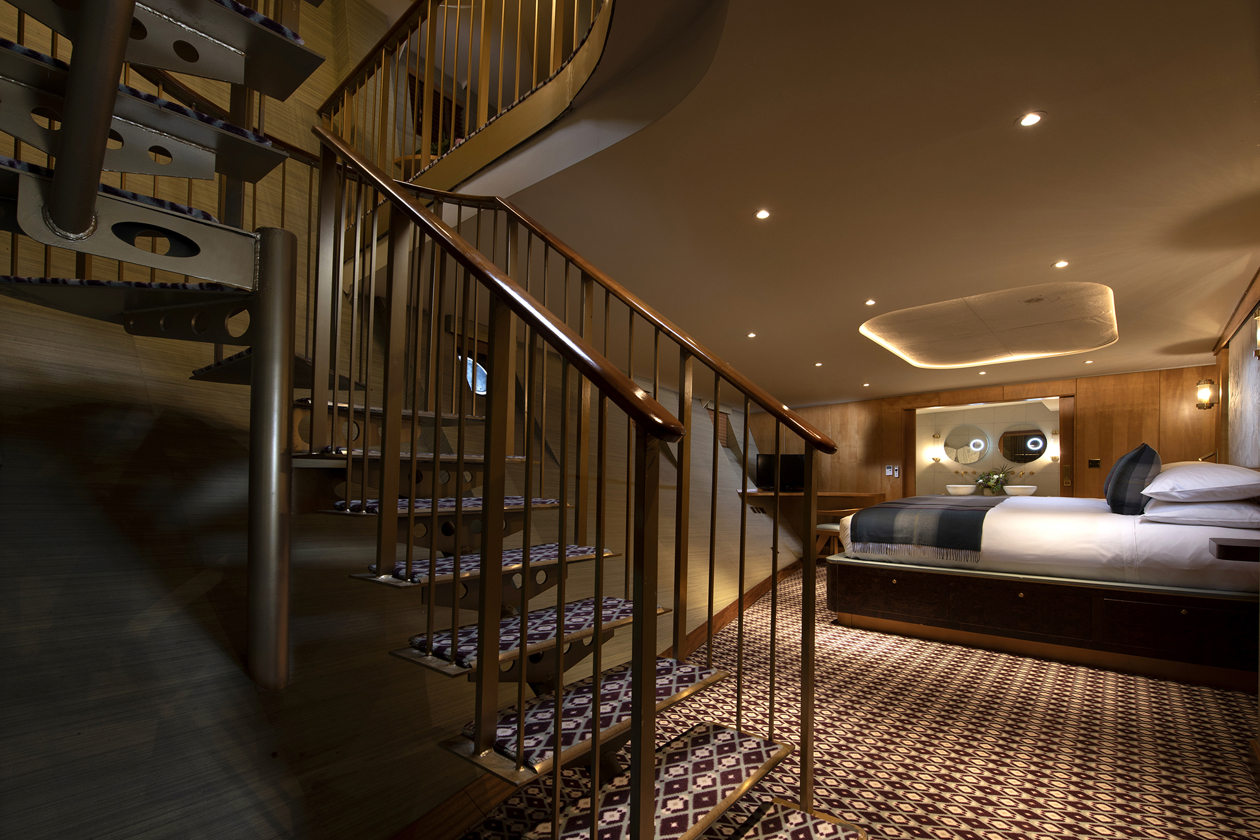 Luxury duplex suite bedroom aboard Fingal hotel Edinburgh, featuring spiral staircase, bespoke wood interiors, patterned flooring, and a beautifully appointed king-size bed.