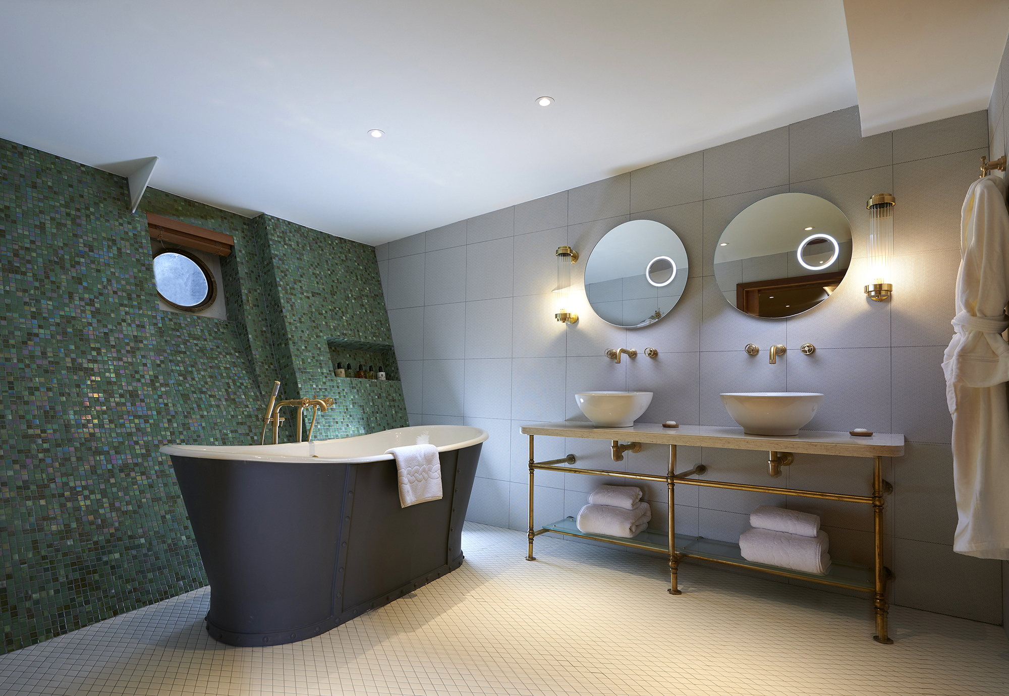 Spacious luxury bathroom aboard Fingal, an Edinburgh hotel on the water, featuring a freestanding bath, double vanity with brass fittings, circular mirrors, and refined nautical-inspired design details.
