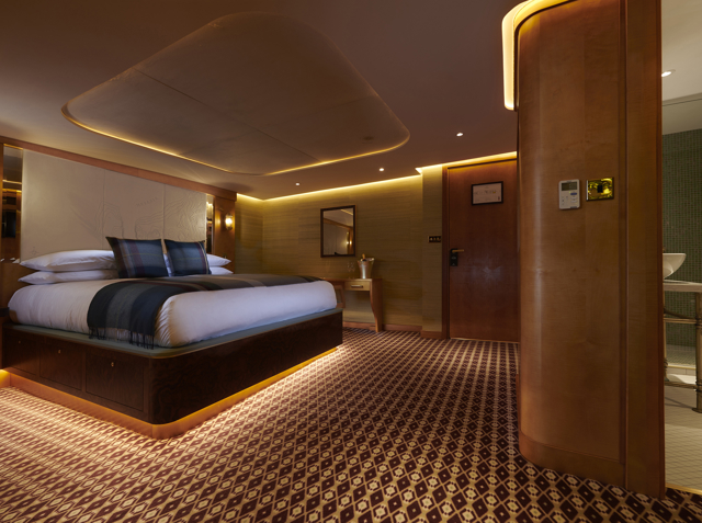 Image of a luxurious cabin with the bed neatly made and a warm dark atmosphere. 