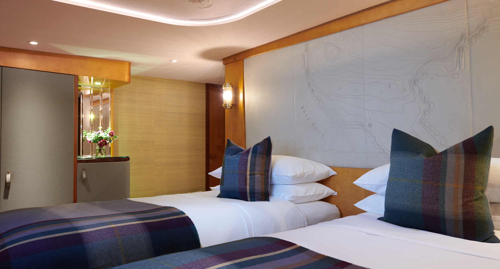 Twin beds in a cabin, white bedding and purple and navy tartan blanket and cushion on each bed