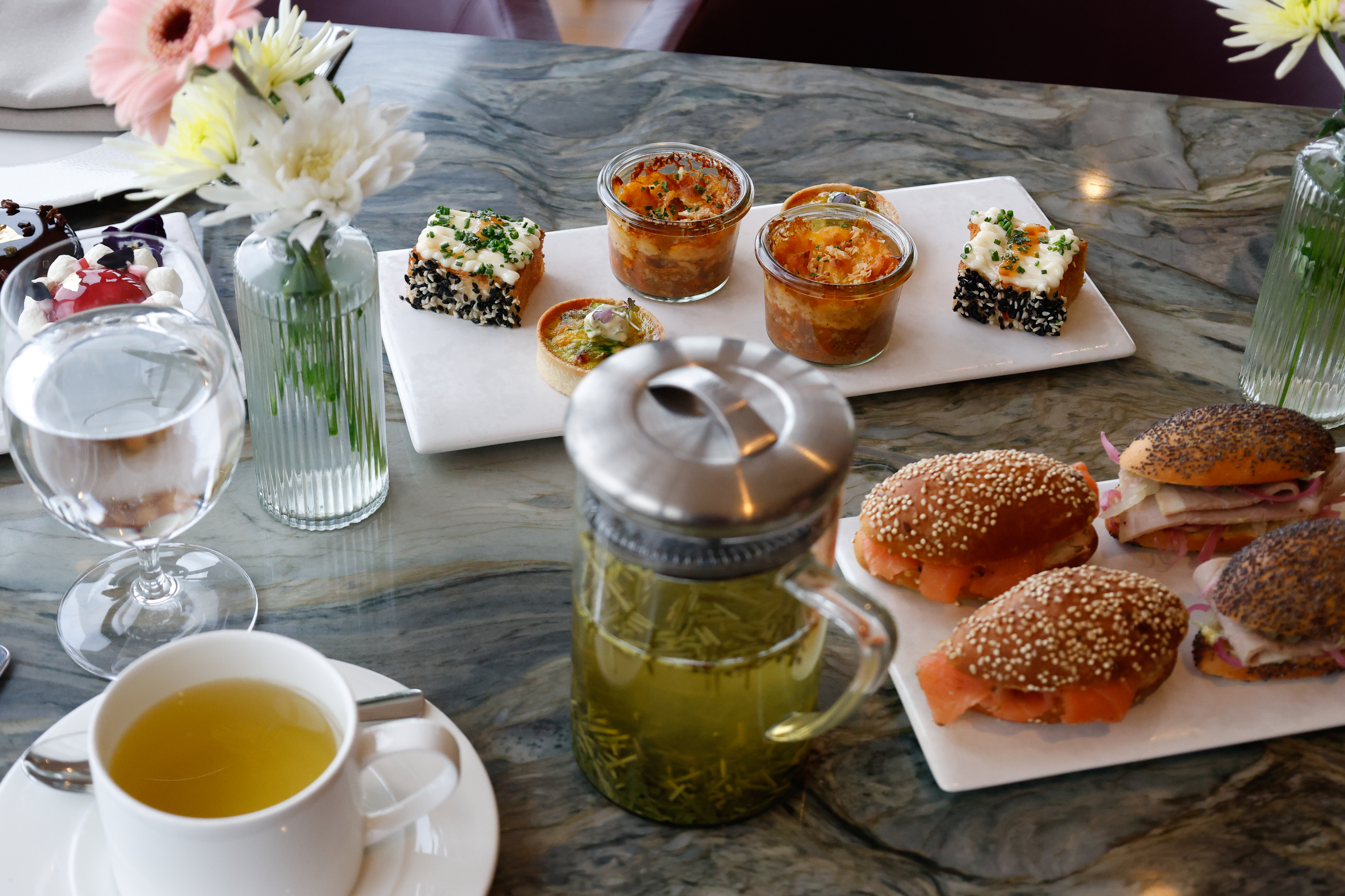 Savoury delicacies and navettes on the table for afternoon tea, with two clear vases with flowers and a teapot